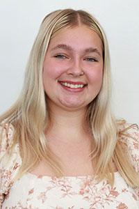 woman with platinum blonde hair wearing a cream floral shirt with pink flowers